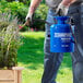A person holding a blue metal Chapin sprayer and watering a plant.