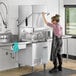 A woman in a black apron loading plates into an Ecoline by Hobart electric door-type dishwasher on a counter in a professional kitchen.