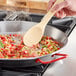 A person stirring food in a Vigor carbon steel paella pan with a wooden spoon.