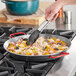 A person cooking food in a Vigor carbon steel paella pan on a stove.