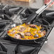 A person cooking food in a Vigor enameled carbon steel paella pan on a stove.