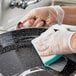 A person cleaning a Vigor enameled carbon steel paella pan with a sponge.