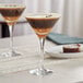 Two Acopa Select martini glasses filled with a drink on a table.