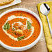 A bowl of Chef Francisco tomato basil soup with basil leaves and croutons on a table.