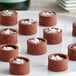 A close-up of a brown dessert with a La Rose Noire mini chocolate tart shell filled with white topping.