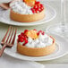 A white plate with a La Rose Noire large round vanilla tart shell with whipped cream and red berries on it.