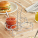 A metal wire condiment holder with a jar of sauce next to a burger.