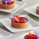 A group of La Rose Noire medium round graham cracker tart shells filled with small desserts on white plates with strawberries.