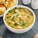 A bowl of Chef Francisco Italian-Style Wedding Soup with meatballs and vegetables next to bread rolls.