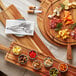 An Acopa XL acacia wood serving board with cheese, crackers, and utensils on a wood surface.