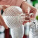 A person pouring whiskey from an Acopa Cut Glass Sphere Whiskey Decanter into a glass.