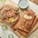 An Acopa round acacia wood serving board with bowls of food and a bowl of shrimp on a table.