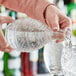 A person using an Acopa Cut Glass Whiskey Decanter to pour water into a glass.