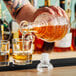 A person pouring a glass of brown liquid from an Acopa Cut Glass Whiskey Decanter.