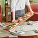 A person holding an Acopa XL acacia wood serving tray with food on it.