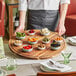 A waiter holding an Acopa acacia wood serving board with food on a table.