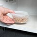 A hand holding a Pactiv translucent plastic deli container filled with food.