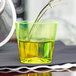 A person pouring liquid into a neon yellow Fineline Quenchers hard plastic shot cup on a table in a cocktail bar.