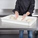 A person in a chef's uniform and gloves using a white Cambro pizza dough proofing box to hold dough.