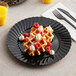 A WNA Comet black plastic plate with waffles, berries, and whipped cream.