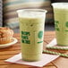 A cup of green liquid in a New Roots PLA compostable plastic cup on a table.