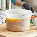 A hand using a measuring cup to pour liquid into a large white Carlisle food storage container.