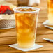 A clear plastic cup filled with iced tea and ice cubes, placed on a white coaster.