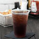 A clear Dart plastic cup filled with iced tea on a table.