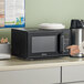 A person pointing at a black Galaxy office series microwave on a counter.