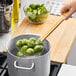 A person using an Emperor's Select fine skimmer with a bamboo handle to stir a pot of brussels sprouts.