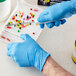 A hand wearing a blue Showa biodegradable nitrile glove cuts pills on a white surface.