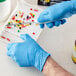 A hand wearing a Showa blue biodegradable nitrile glove using a knife to cut pills on a white surface.