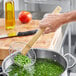 A person using an Emperor's Select bamboo skimmer to stir peas in a pot.