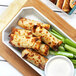 A plate of chicken and celery sticks with a bowl of white liquid on a table.