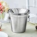 An Acopa stainless steel wine tasting spittoon on a table.