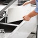 A person holding a white rectangular Regency Polyboard underbar sink cover.