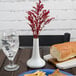 A white CAC porcelain bud vase with red flowers on a table.