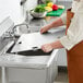 A person in an apron using a Regency stainless steel sink cover to cut something on a counter in a professional kitchen.