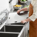 A man in an orange apron cutting a stainless steel sheet on a counter.