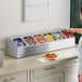 A woman standing at a counter with a ServSense stainless steel hotel pan organizer with containers of condiments in it.