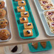 A green Cambro fiberglass market tray filled with pastries on a table.