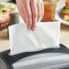 A hand using a white Tork Universal interfold dispenser napkin with a black plastic handle.