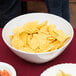 A white round melamine catering bowl filled with chips on a table.