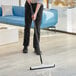 A person using a Lavex white double neoprene floor squeegee with a metal handle to clean the floor.