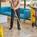 A person using a Lavex rubber floor squeegee with a wood handle to clean the floor