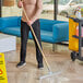 A man using a Lavex rubber floor squeegee with a wood handle to clean a floor.