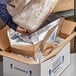 A person holding a large bag of brown material with a box of bread inside.