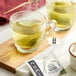 A pair of glass cups of Numi Kukicha tea with tea bags in them.