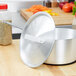 A silver Vollrath Arkadia pot with a lid on a wooden table.