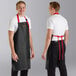 Two men wearing CrewSafe black and red vinyl aprons with red straps in a professional kitchen.